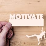 A paper cutout of a climber reaching the word Motivate. Business concept