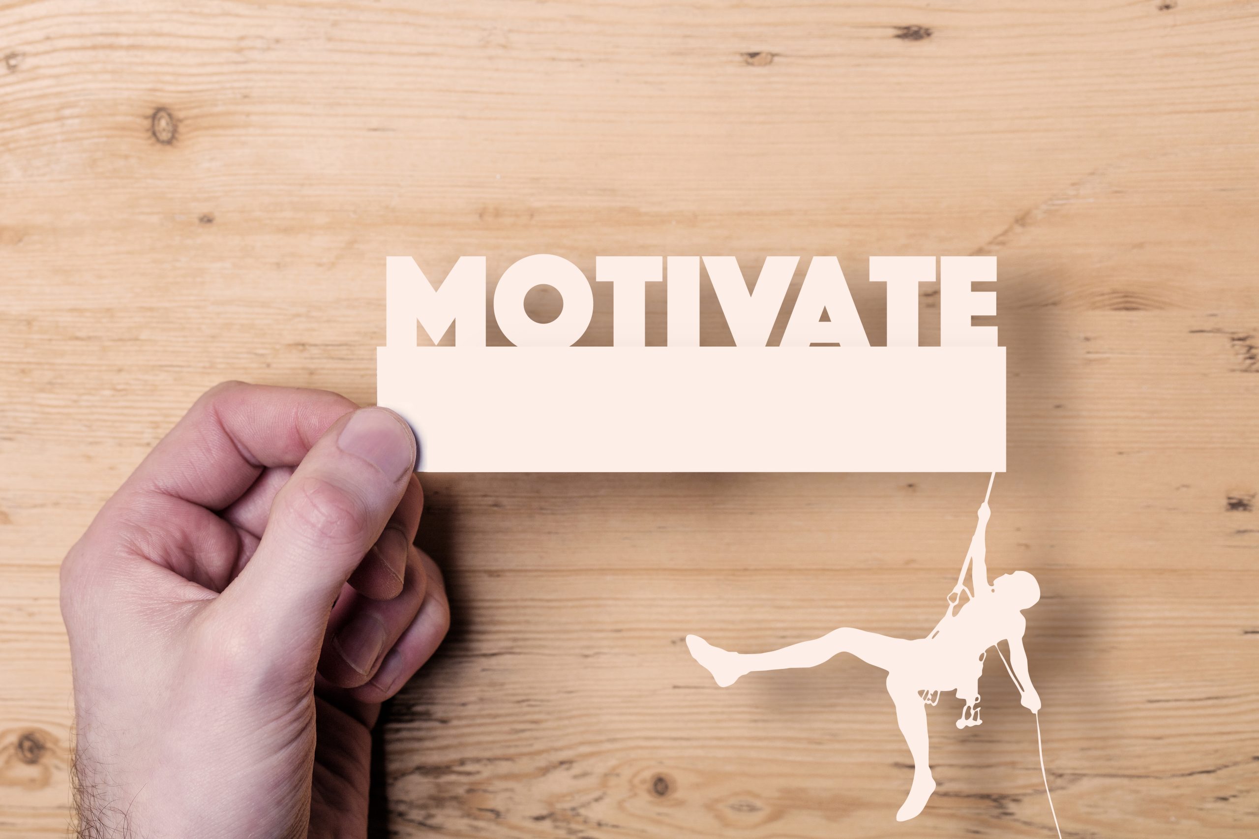 A paper cutout of a climber reaching the word Motivate. Business concept